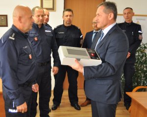Burmistrz Miasta Radzyń Podlaski Pan Jerzy Rębek przekazuje na ręce komendanta urządzenie do badania stanu trzeźwości w obecności innych policjantów.