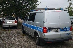 Samochód marki Opel Astra stoi na szutrowym parkingu a za nim oznakowany radiowóz policyjny